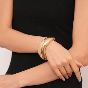 Close-up of polished gold wide metal cuff bracelet with a modern irregular twisted design