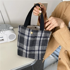 Detail of checkered woolen tote bag featuring a black woven handle and metal snap closure