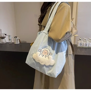 Blue canvas tote bag with 3D plush cloud sheep embroidery worn by a model in a cafe