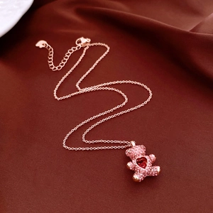 Close-up of rose gold teddy bear pendant with pink stones and red heart on velvet