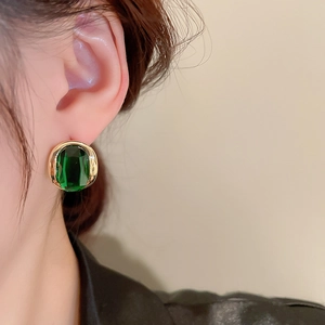 Close-up of a model wearing a gold-plated earring with a green emerald zircon stone