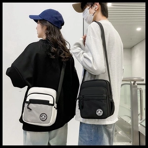 Detail of minimalist crossbody bags in black and cream worn by couple on street