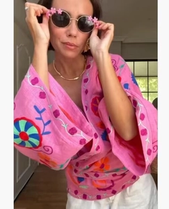 Close-up of pink loose cardigan with colorful floral embroidery and flower-rimmed sunglasses