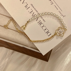 Detail of camellia pearl bracelet with gold chain and crystals on white silk background