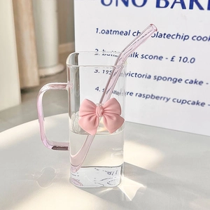 Square glass water cup with pink bow decor, handle and straw on a cafe table