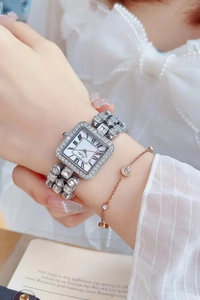 Close-up of square silver watch with rhinestones and Roman numeral dial on a wrist