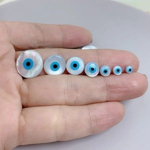 Detailed comparison of various sizes of mother of pearl evil eye beads on a hand