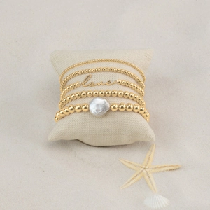 Bohemian gold beaded bracelet set with love charm and baroque pearl on beach sand background