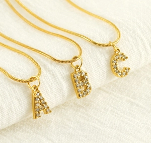 Close-up of gold snake chain necklaces with zircon-encrusted A, B, and C pendants