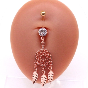 Détail macro du piercing de nombril en or rose avec pendentif attrape-rêves