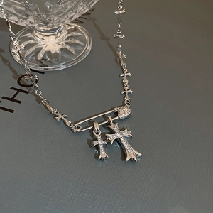 Detail of silver safety pin and double cross pendant necklace with zircon inlay
