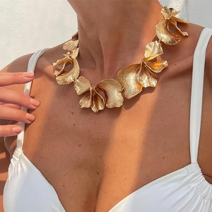 Macro detail of golden metal flower petal collar necklace on model with soft lighting