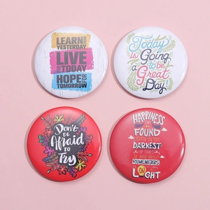 Set of four round tinplate brooches with inspirational English quotes and colorful art