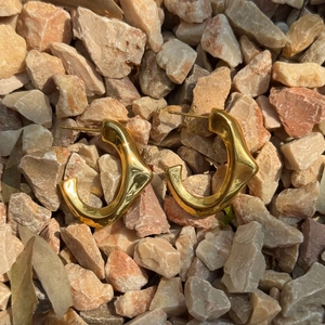 Close-up of golden wavy geometric earrings on natural light stones with sun reflections