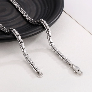 Detail of silver stainless steel chain necklace with square links on black plate