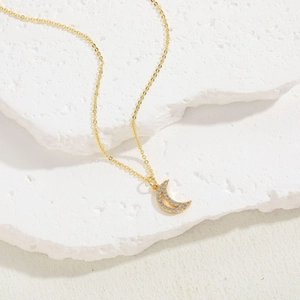 Detail of gold crescent moon pendant with micro-pave white zircon on stone background