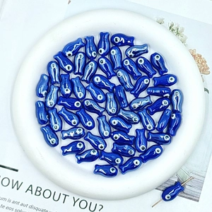 Macro detail of glossy dark blue ceramic fish beads for DIY jewelry making in a white bowl