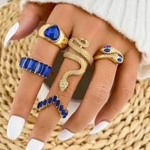 Detail of gold snake and blue gemstone ring set worn on hand over a straw mat