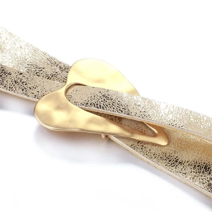 Close-up of gold heart buckle with metallic finish on gold textured leather bracelet