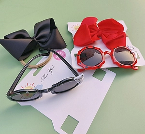 Detail view of wave-edge children's sunglasses set with oversized bows on a card