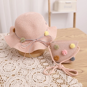 Detail of pink straw hat and bag set for kids with colorful pom-poms and ribbon bow