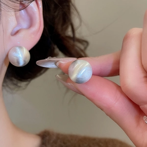 Detailed view of silver spherical stud earrings with cat eye stone texture on model ear