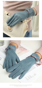 Detail of warm grey-blue suede gloves featuring elegant bow decoration and wavy stitching