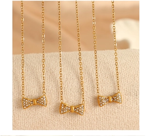 Macro de trois colliers dorés avec pendentifs nœuds en zircon sur tissu blanc
