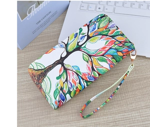 Detailed view of long zip wallet with colorful tree pattern and wrist strap on a desk