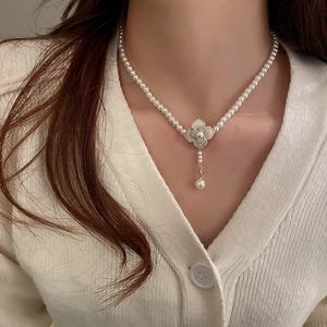 Close-up of pearl necklace featuring a gold four-leaf clover pendant and pearl tassel drop