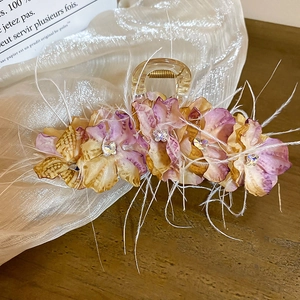 Détail d'une pince à cheveux avec fleurs en satin, strass et plumes blanches