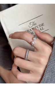 Close-up of elegant silver zircon paved ring and open pearl ring on model's finger