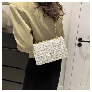 Close-up of woven white and gold tweed texture with a golden rotary lock and chain strap
