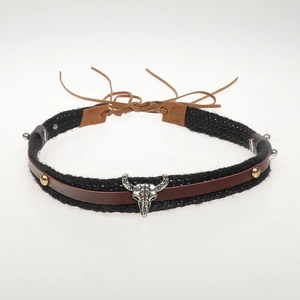 Close-up of black braided cord with silver bull skull pendant and brass stud accents