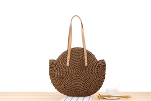 Detailed view of brown round straw woven bag with faux leather handles on wooden surface