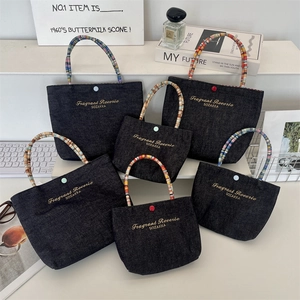 Detail of dark blue denim mini tote bags with colorful woven handles and embroidery