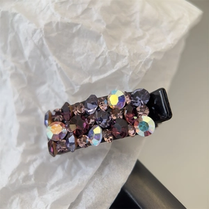 Détail d'une petite barrette à cheveux avec strass violets et irisés sur base noire