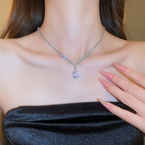 Detailed close-up of a silver necklace featuring a pink teardrop gemstone and small diamonds