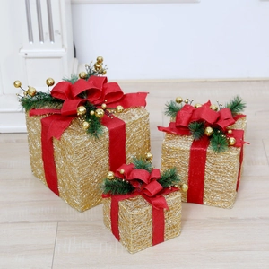 Close-up of three lighted Christmas gift boxes with gold mesh and red bows on wood floor