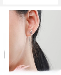 Silver snake earring with green gemstone eyes and long tassels on a model's ear