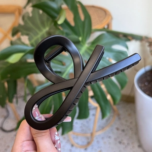 Close-up of matte black bow-shaped hair claw clip held by hand in a lifestyle setting