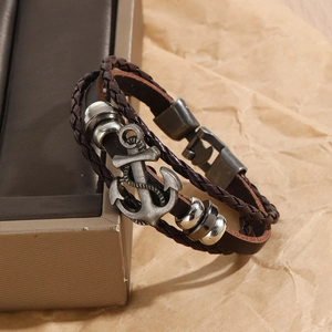 Detail of vintage anchor charm on braided brown leather bracelet with metal accents
