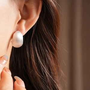 Detail of matte translucent white C-shape stud earring on ear with soft light effect