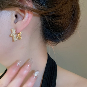 Close-up of star-shaped gold earrings with sparkling pavé zircons worn on ear