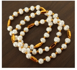 Three freshwater pearl bracelets with gold cylinder beads on dark wood background