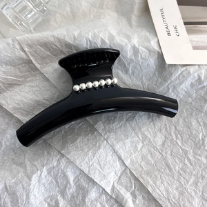 Detail view of a large black hair claw clip featuring elegant white pearl embellishments