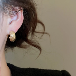 Close-up of golden woven texture C-shape earrings worn on the ear showing elegant details