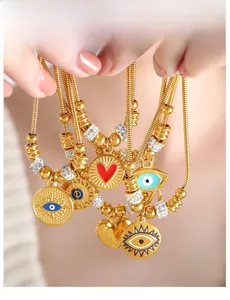 Detail of 18k gold plated snake chain bracelet featuring evil eye and heart charms