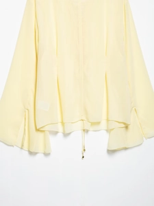 Détail du chemisier jaune clair à col en V montrant les manches cloche et le cordon