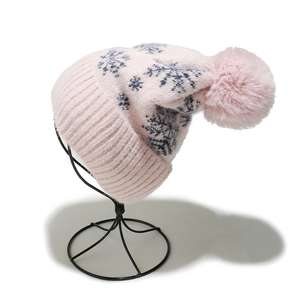 Close-up of pink knit winter hat featuring blue snowflake patterns and a large fluffy pom-pom